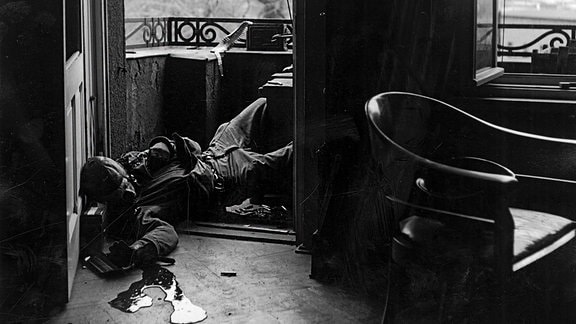 Schwarz-Weiß-Bild: Ein verwundeter Mann liegt in einem Balkon-Durchgang.