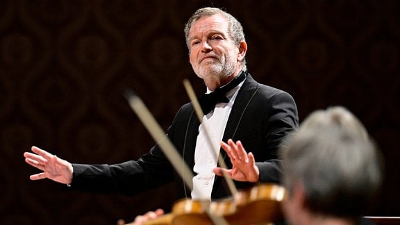 Porträt Christophe Rousset: Ein Mann mit Fliege und Anzug dirigiert ein Orchester.