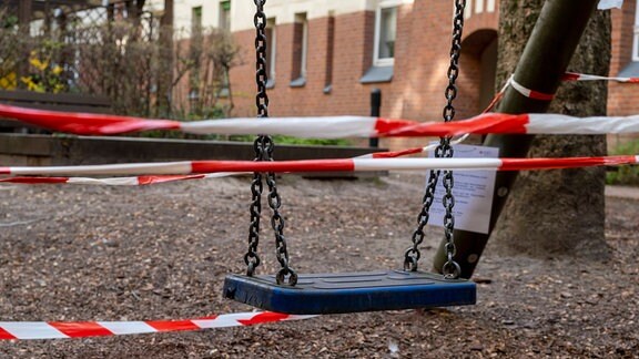 Mit rot-weißem Absperrband abgesperrter Kinderspielplatz auf einem Hof eines Wohnhauses.