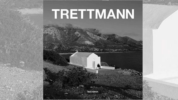 Cover des neuen Trettmann-Albums "Insomnia": schwarz-weiß-Foto eines weißen Hauses inmitten einer hügeligen Landschaft an der Küste. Auf den Stufen des Hauses sitzt ein Mann komplett in Schwarz gekleidet.