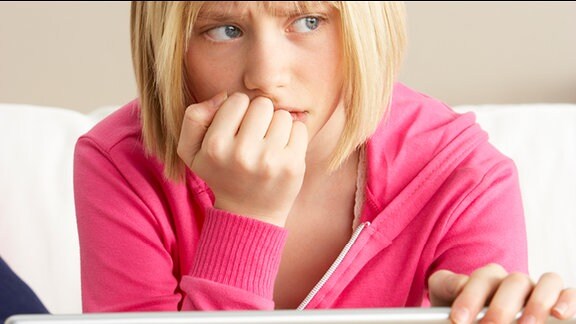 Ein Mädchen sitzt traurig an einem Laptop.
