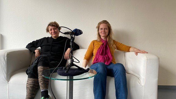 Zwei Frauen sitzen auf einer Couch mit einem Mikrofon vor ihnen.