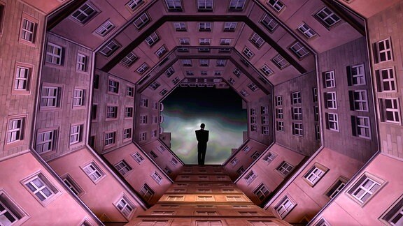 Eine Personen steht auf eine Bühne, die wie ein Blick von oben in einen Innenhof gestaltet ist.