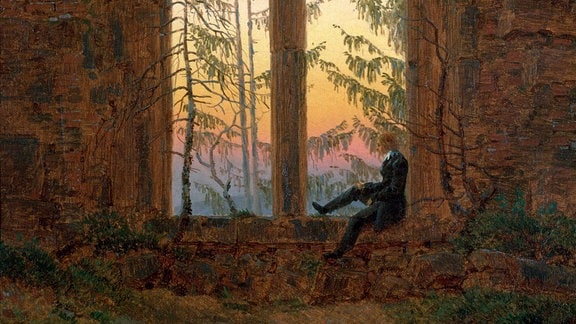 Gemälde einer Ruine von Caspar David Friedrich: Durch die hohen Spitzbogenfenster ist ein gelb-orange-gefärbter Himmel zu sehen, ein Person sitzt in einem der Fenster.