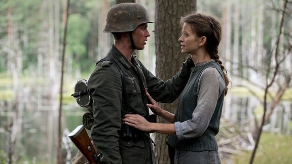 Ein Soldat in Uniform steht in einem Wald vor einer Frau und umarmt sie.  