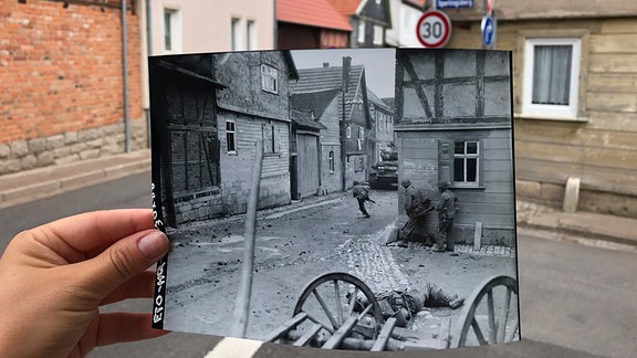 Eine Hand hält ein schwarzweiss Foto an einer Straßenecke.