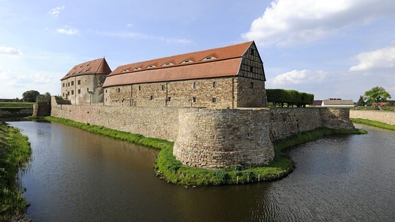 Die Wasserburg Heldrungen, umgeben von Wasser befindet sich ein Gebäudekomplex aus Steinen hinter einer Burgmauer. 