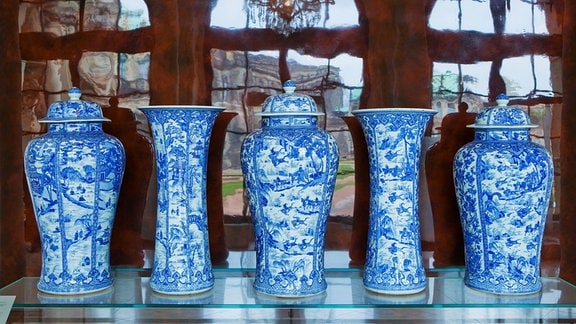 Fünf blau-weiße Porzellangefäße mit asiatischen Motiven stehen in einer Reihe.