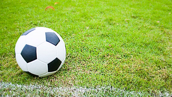 Ein groß zu sehender Fußball liegt auf dem Rasen.