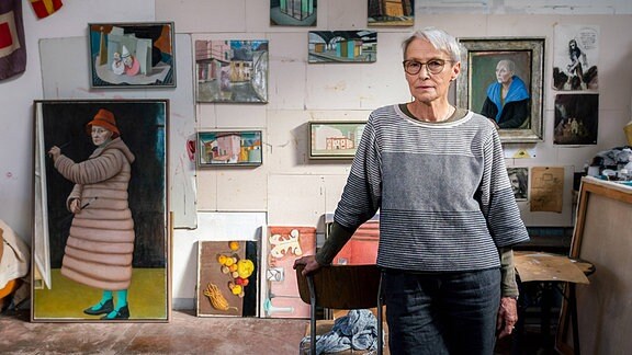 Doris Ziegler in ihrem Atelier: Eine Frau steht vor einer Wand mit zahlreichen Gemälden.