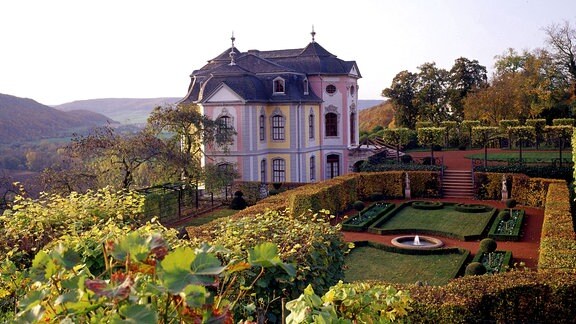 Blick auf ein kleines Schloss in einem Park, im Hintergrund das Saaletal 