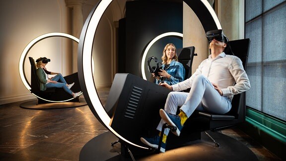 Menschen sitzen in VR-Bikes, die wie ein großer Kreis aussehen, der längs beleuchtet ist