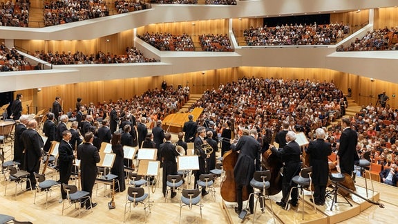 Das Dresdner Festspielorchester, mehrere schwarz gekleidete Musikerinnen und Musiker mit ihren Instrumenten stehen auf der Bühne des Dresdner Kulturpalasts.