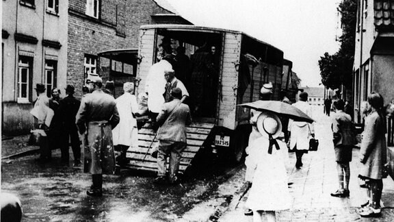 Schaulustige sehen 1942 zu, wie die Polizei Jüdinnen und Juden zur Deportation auf Lastwagen verlädt