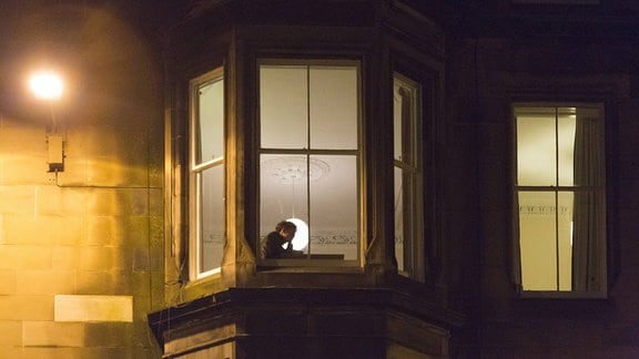 einsamer Student lernt nachts an einem beleuchteten Fenster in Edinburgh