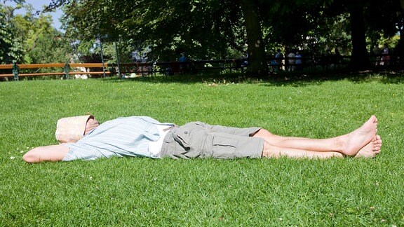 Ein  Mann liegt auf einer Wiese und ruht. Über sein Gesicht hat er als Sonnenschutz einen faltbaren Stadtplan gelegt.