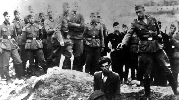 Ein Soldat der Einsatzgruppe D ist im Begriff, 1942 einen Juden zu erschießen, der an einem teilweise gefüllten Massengrab in Vinnitsa, Ukrainische SSR, Sowjetunion, niederkniet. 