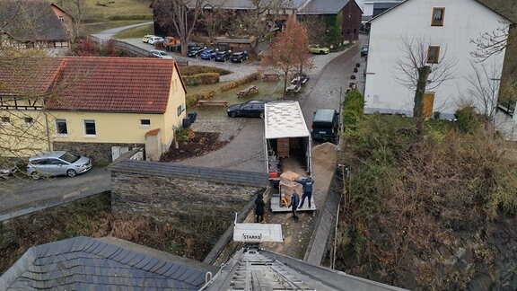 Menschen laden aus einem Laster Kisten auf einen Leiter-Aufzug.