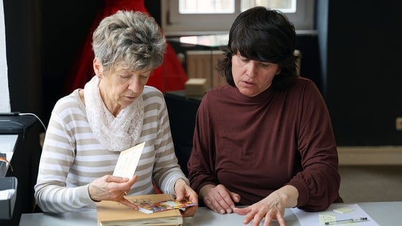 Zwei Frauen sitzen an einem Tisch und sortieren Unterlagen