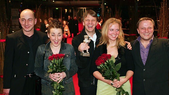 Drei Männer und zwei Frauen bei einer Filmpreisverleihung. Sie halten den Preis und Blumen in der Hand und strahlen.