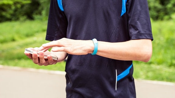Fitness-Überwachungsarmband am Handgelenk eines Mannes der sein Smartphone bedient.