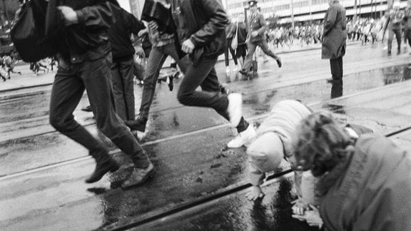 Auf dem Foto von Martin Jehnichen ist die Demonstration zum 40. Jahrestag der DDR am 7.10.1989 zu sehen – vorn eine stürzende Mutter mit Kind auf Karl-Marx-Platz (Leipzig)