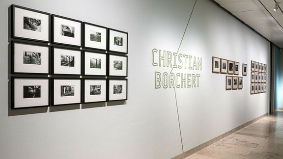 Blick auf eine Wand in einer Ausstellung mit zahlreichen kleinen Bildern und dem Schriftzug Christian Borchert.