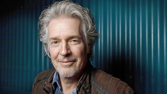 Autor Frank Schätzing mit grauen Haaren  und Bart in einer braunen Lederjacke