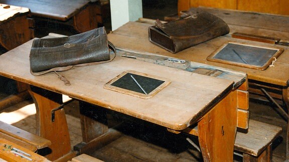 Historisch Ranzen und Schiefertafeln liegen auf alten Schulbänken