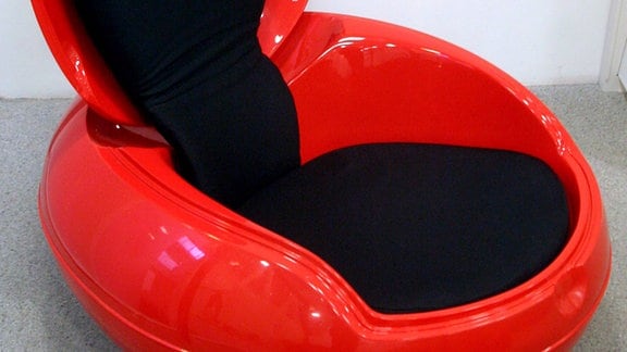 Sitzei - rotes, eiförbiges Gebilde aus Plastik, mit geöffneter Klappe die als Lehne dient
