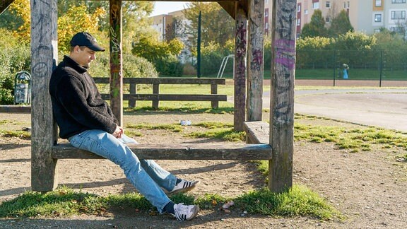 Ein Mann mit Jeans und Cappy sitzt in einem alten Holzgerüst.