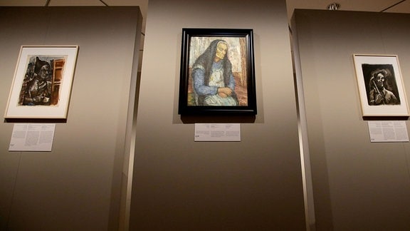 Porträt-Gemälde hängen in einer Ausstellung an einer Wand.