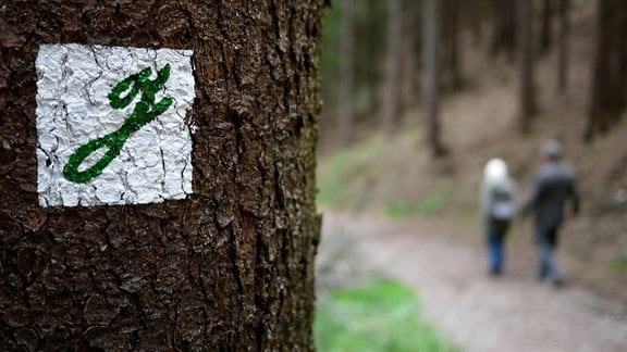 Zwei Wanderer gehen an einem Baum mit dem aufgemalten Buchstaben "g" vorbei.