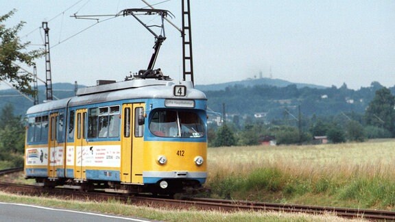 Eine alte gelbe Straßenbahn fährt an einem Feld vorbei. Vor oben ist ein Schild mit einer "4" zu erkennen.