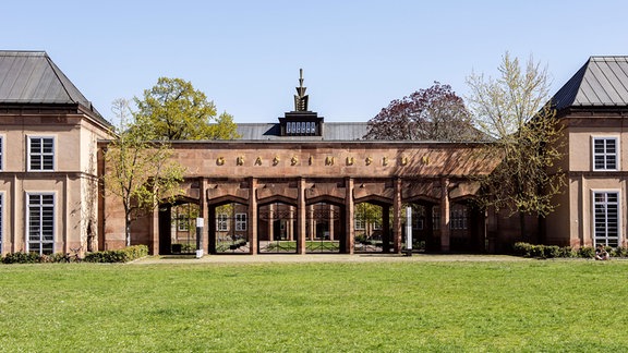 Ein imposantes Tor mit mehreren Torbögen und der Aufschrift Grassimuseum erstreckt sich zwischen zwei Gebäudeteilen.