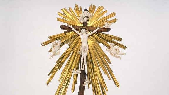 Eine geschnitzte Skulptur aus teilweise farbig angemaltem Holz zeigt Engelfiguren um einen gekreuzigten Jesus.