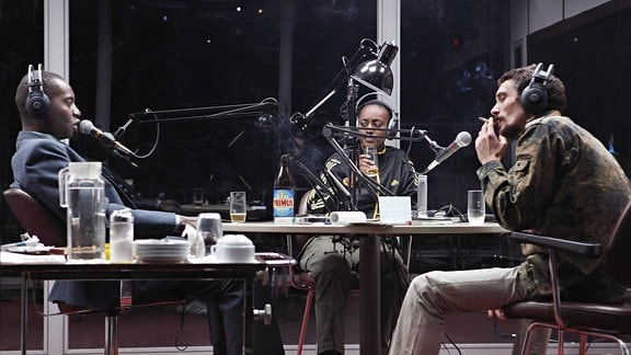 3 Personen sitzen in einem Tonstudio.