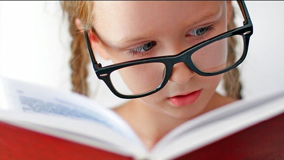 Ein Mädchen mit einer großen Brille ließt in einem Buch