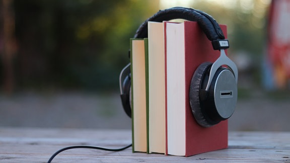 Kopfhörer umschließen einen Bücherstapel wie einen Kopf