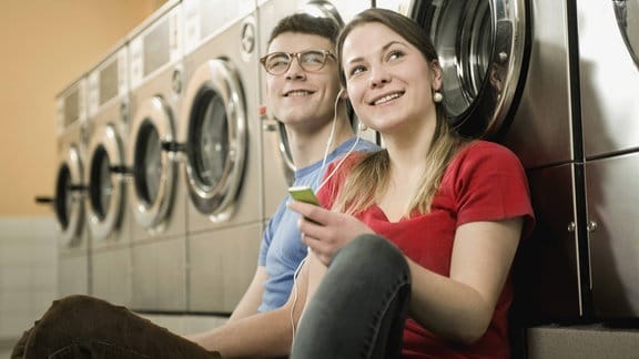 Ein Junges Paar sistzt mit MP3 -Player und Kopfhörern im Waschsalon.