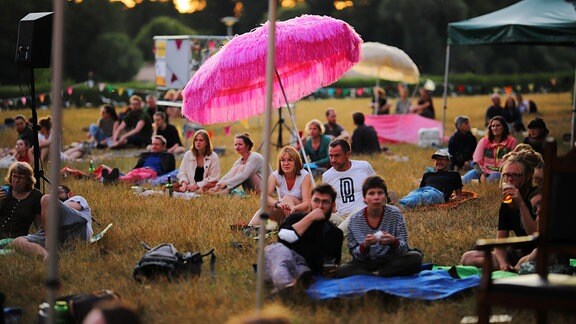 Menschen picknicken auf einer Wiese beim Leipziger Hörspielsommer