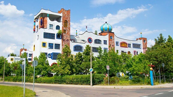 Hundertwasser-Gymnasium in Wittenberg: Ein Gebäude mit wellenföfmigen Dach, bei dem sich weiße Fassade und Ziegelstein-Optik abwechseln.