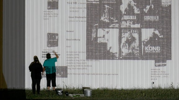 Zwei Personen stehen zusammen vor einer Wand und schauen auf eine große Projektion von Bildern.