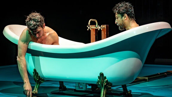 Zwei Männer sitzen im Theaterhaus Jena in einer Badewanne, einer lässt den Arm heraushängen.