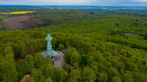 Das Josephskreuz, eine begehbare Konstruktion aus Metall, steht auf dem Großen Auerberg im Harz. Das Kreuz ist aus der Vogelperspektive zu sehen und blau, um das Kreuz herum ist Wald.