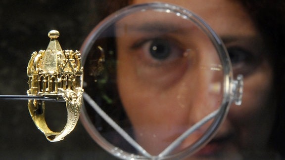 Eine Frau betrachtet mit der Lupe einen goldenen jüdischen Hochzeitsring aus dem 14. Jahrhundert