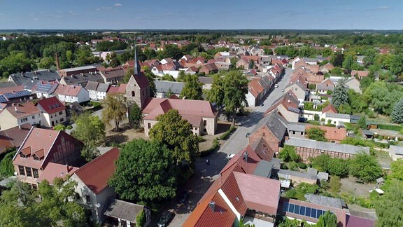 Luftbildaufnahme eines Dorfes, die Dorfkirche sticht markant hervor.