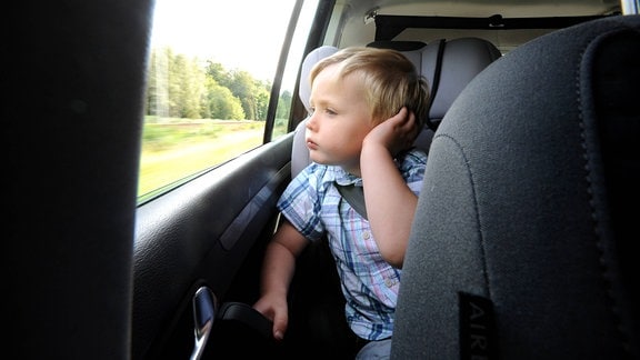 Kleiner Junge sitzt angeschnallt in seinem Kindersitz auf der Rückbank eines Autos.