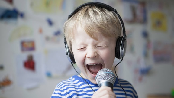 Porträt eines singenden kleinen Jungen mit Kopfhörern und Mikrophon