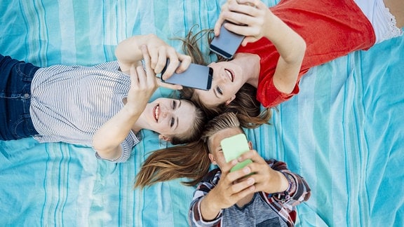 Drei jugendliche Freundinnen mit Smartphones auf einer Decke liegend 